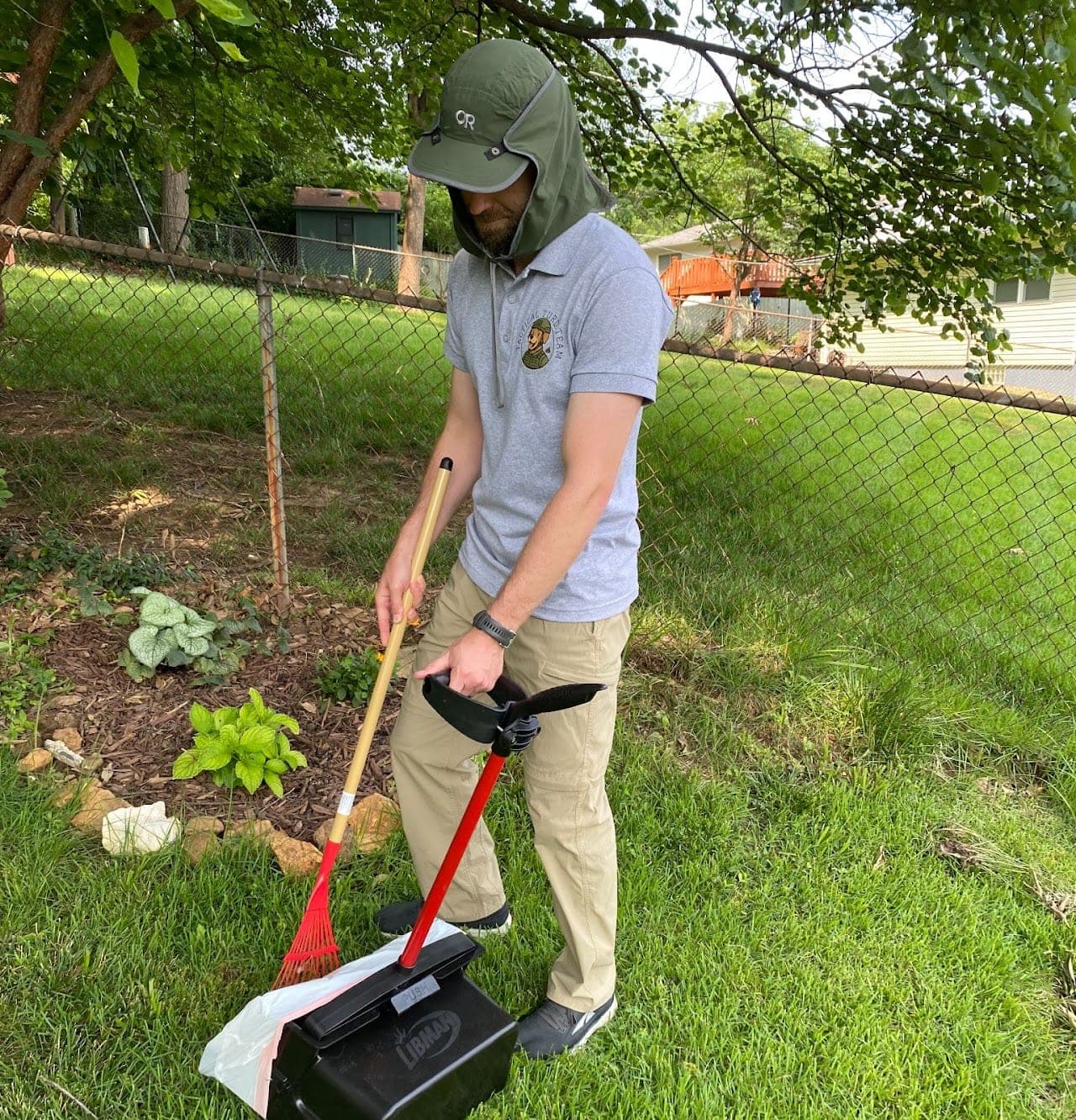 Joel in a Tactical Turd Team shirt and sun hat, working a fenced backyard with the rake in one hand and the pan in the other