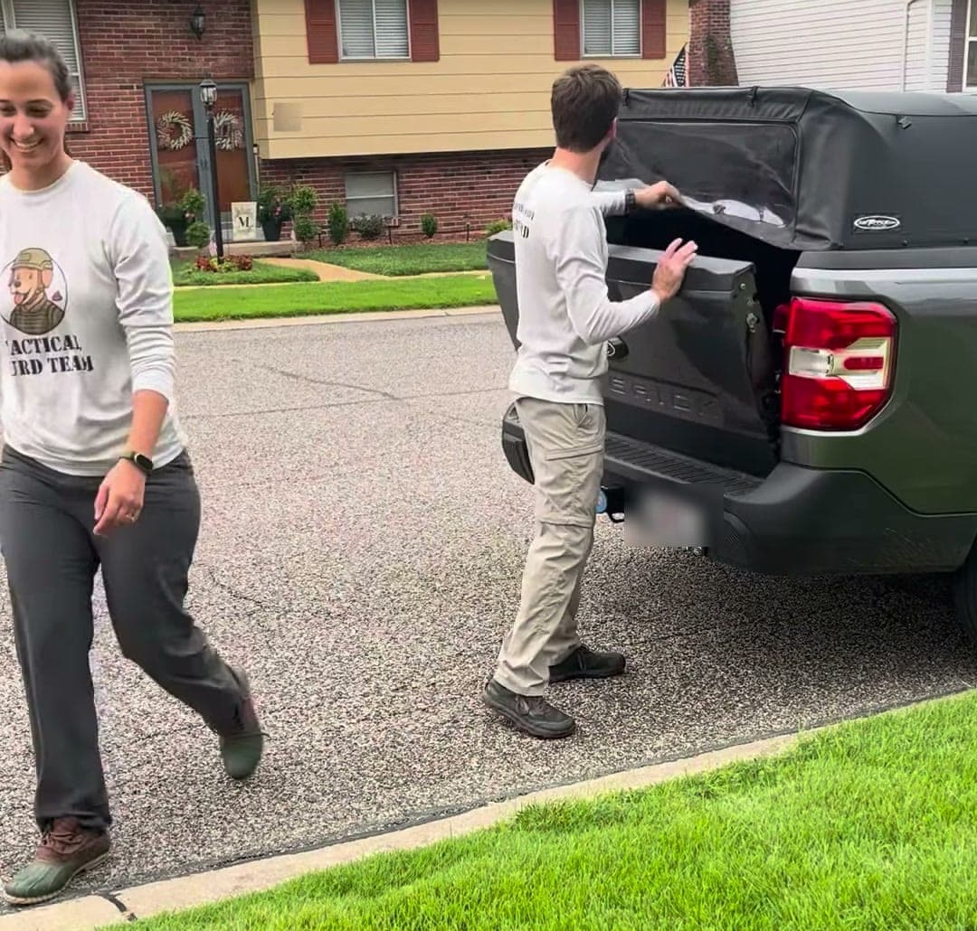 Joel closing the tailgate of their truck while Jessica walks up the driveway, both in Tactical Turd Team shirts